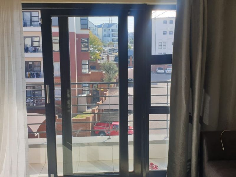 A view from inside looking out through a sliding glass door onto a private balcony with metal railings overlooking the apartment complex.
