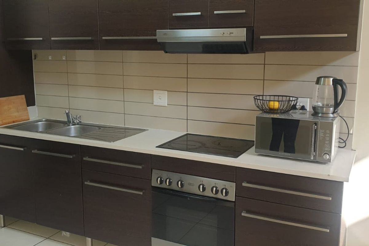 A functional kitchen featuring dark wood cabinetry, a stainless steel sink, built-in oven with electric hob, and a tiled backsplash.