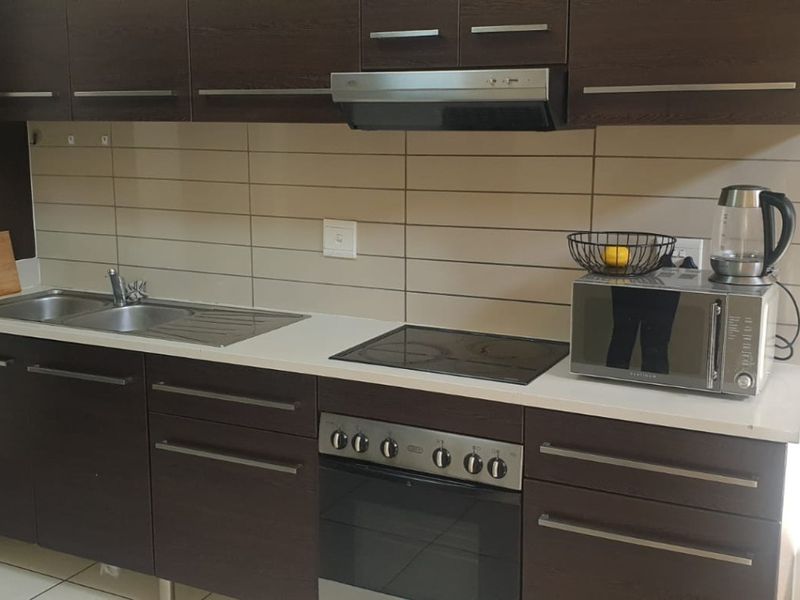 A functional kitchen featuring dark wood cabinetry, a stainless steel sink, built-in oven with electric hob, and a tiled backsplash.