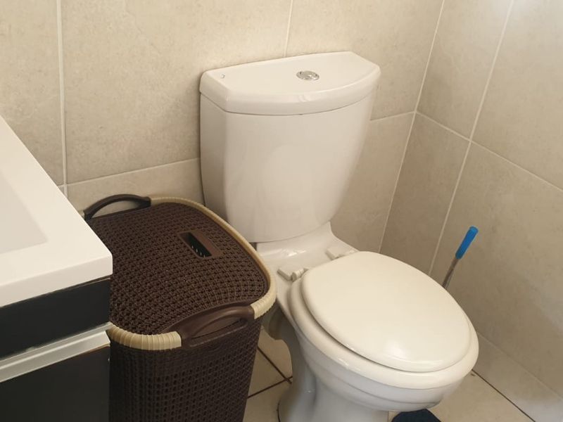 A functional bathroom featuring a standard toilet, vanity basin, and neutral wall and floor tiling.