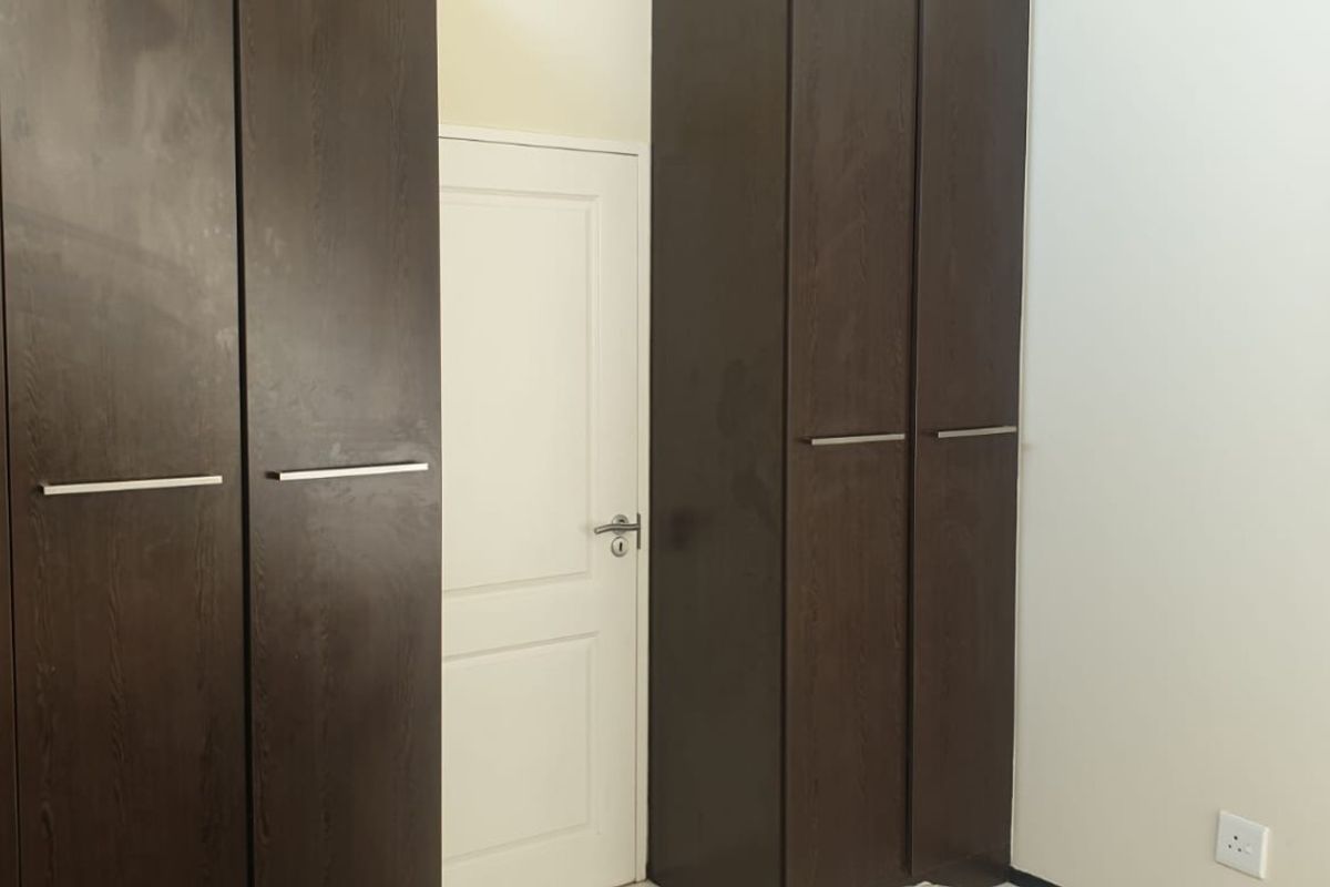 A bedroom interior featuring dark wood built-in cupboards and a white internal door.