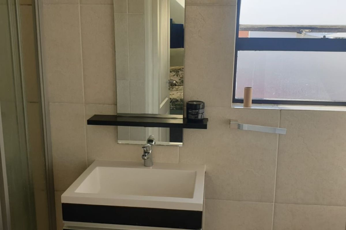 A modern bathroom featuring a vanity basin, wall-mounted mirror, and tiled walls, providing a clean and functional space.