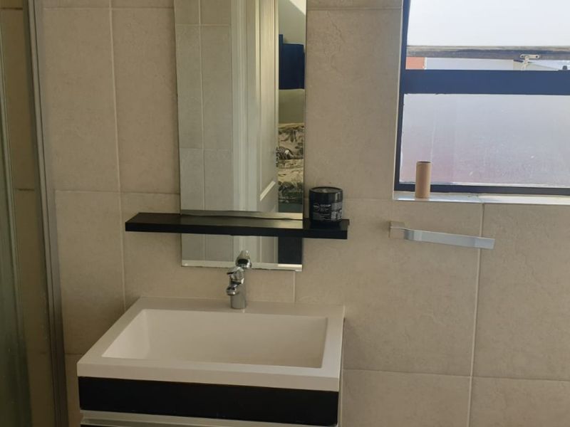 A modern bathroom featuring a vanity basin, wall-mounted mirror, and tiled walls, providing a clean and functional space.