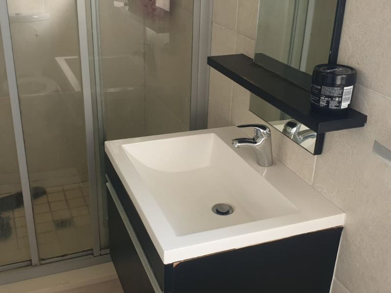 A compact bathroom featuring a modern vanity with integrated basin, chrome mixer tap, and a glass-enclosed shower with neutral wall tiling.