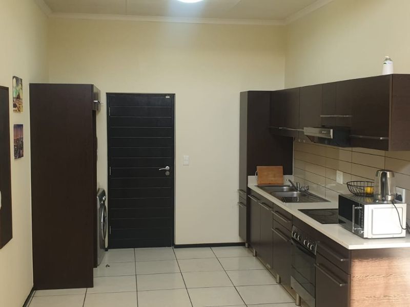 A functional kitchen featuring dark wood cabinetry, built-in oven, hob, extractor fan, and tiled flooring with a clean, modern layout.