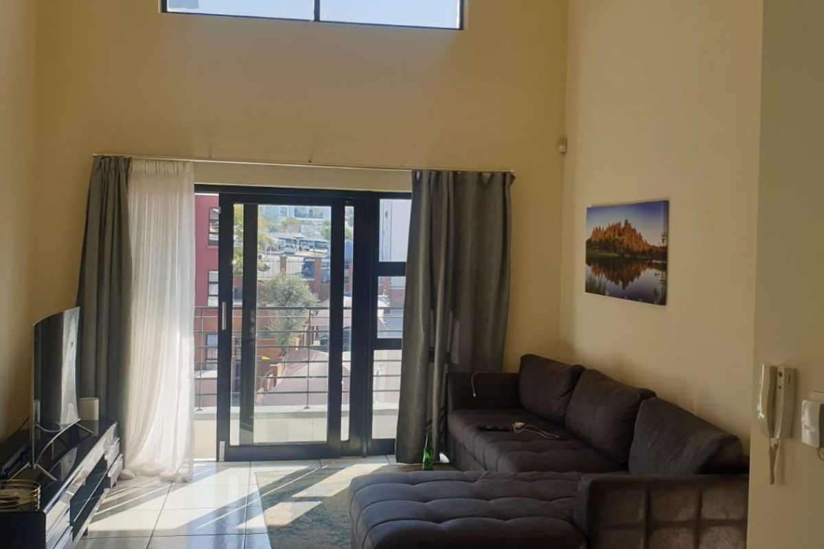 Spacious living room featuring double volume ceilings, a high-level clerestory window, and sliding glass doors leading to a balcony with tiled flooring.