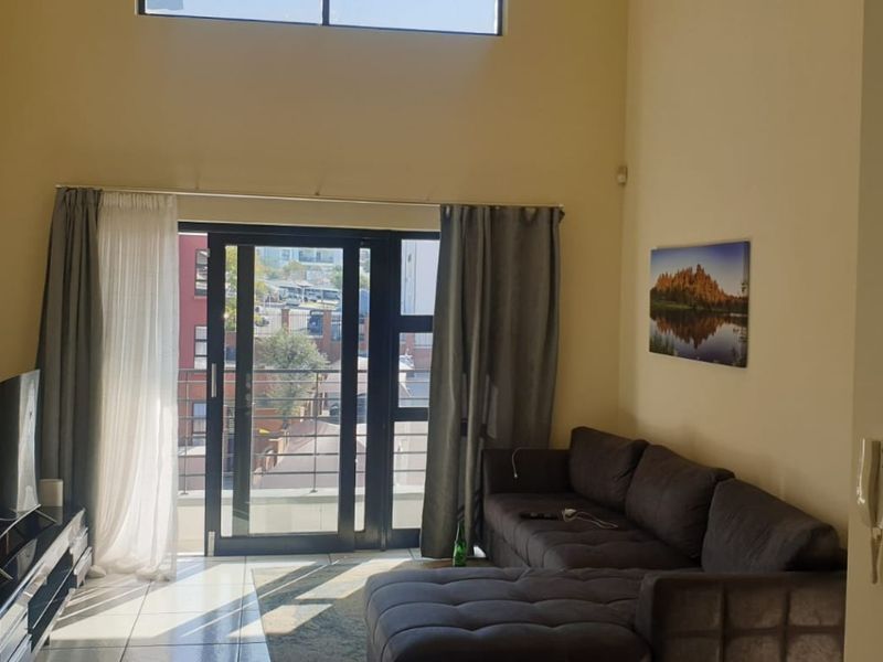 Spacious living room featuring double volume ceilings, a high-level clerestory window, and sliding glass doors leading to a balcony with tiled flooring.