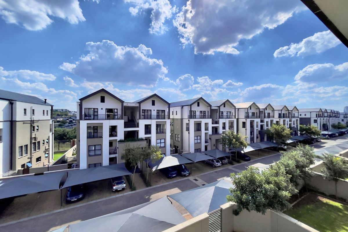 Elevated view of a modern apartment complex featuring multiple residential blocks, covered parking bays, and well-maintained paved driveways.