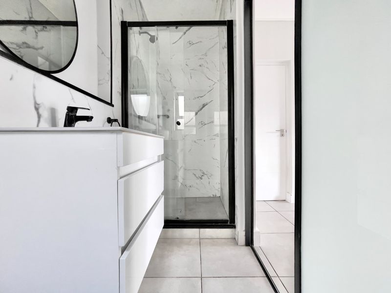 Modern bathroom featuring marble-look wall tiles, a walk-in shower with a sleek black frame, and a contemporary wall-mounted vanity with a black basin mixer.