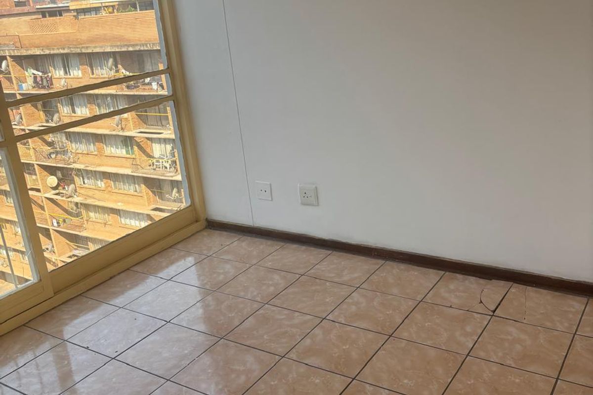 An empty bedroom featuring tiled flooring, a large sliding glass door providing natural light, and neutral wall finishes.
