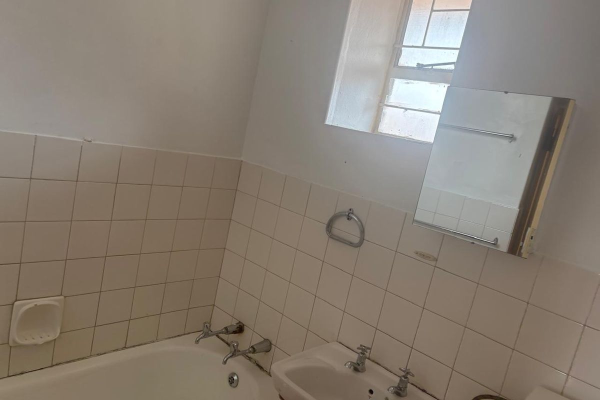A functional bathroom featuring a bathtub, pedestal basin, and wall-mounted mirror cabinet, finished with tiled splashbacks and a window for natural light.