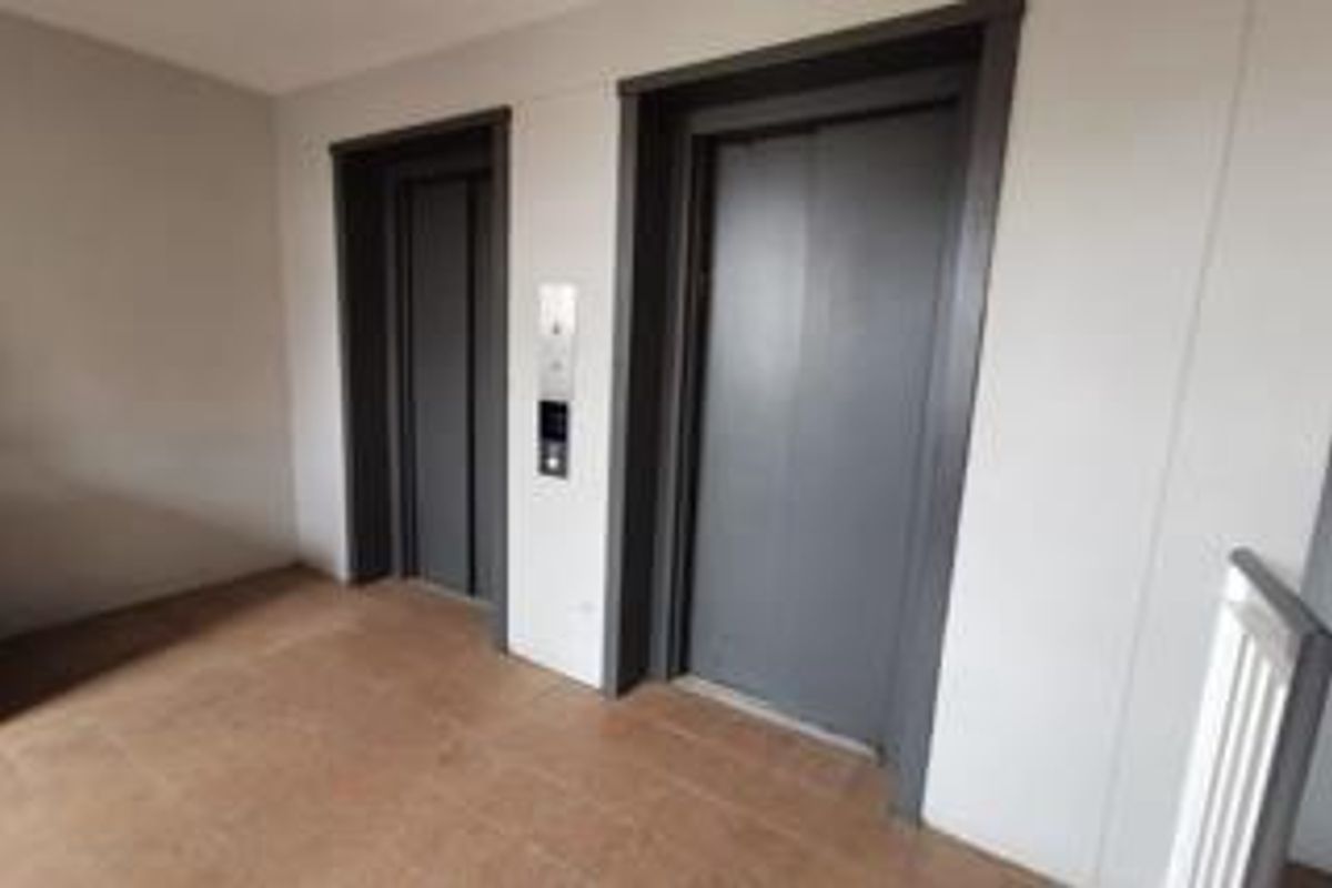 A clean and well-maintained apartment building hallway featuring dual elevators with modern call panels and tiled flooring.