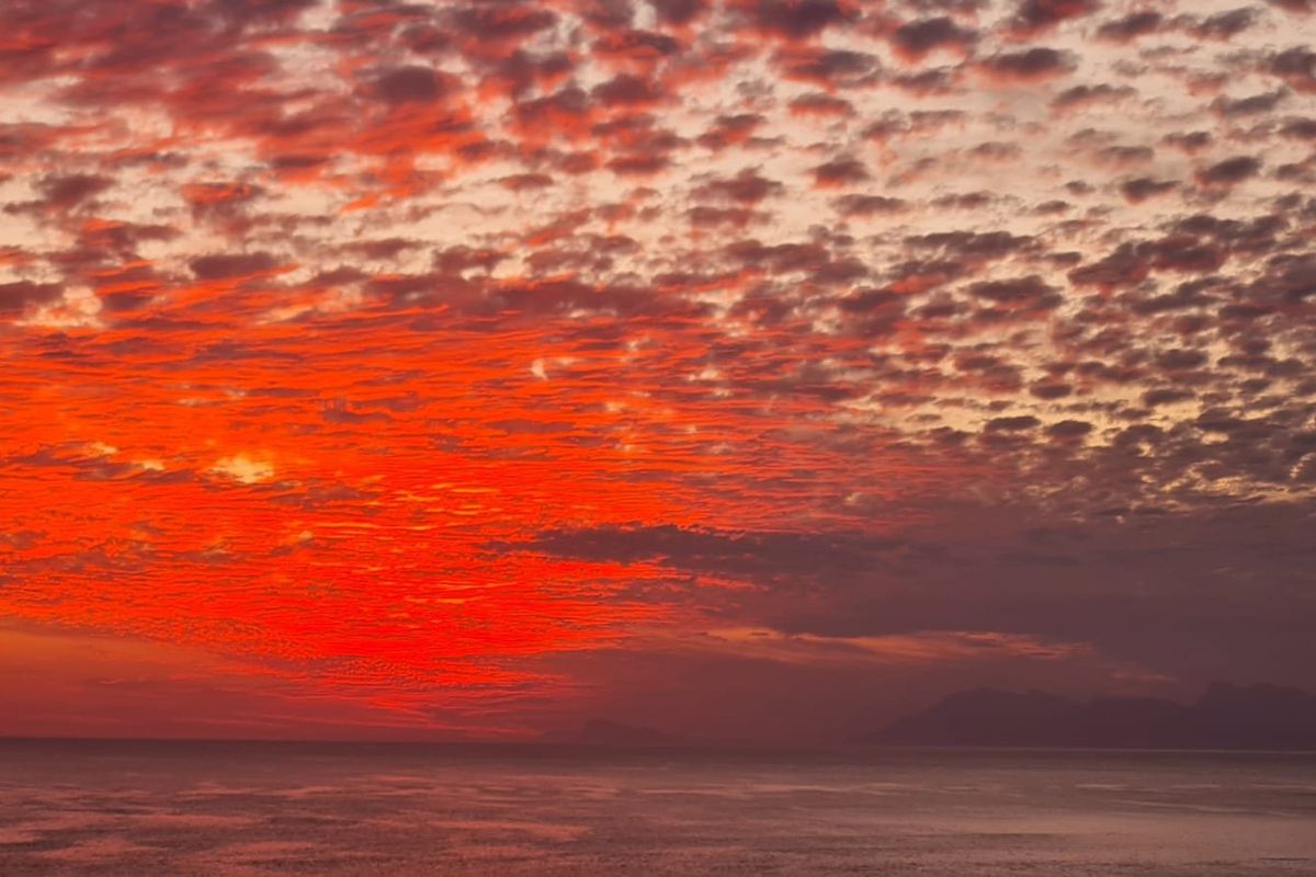 A scenic view of a vibrant sunset over the ocean and distant mountains.
