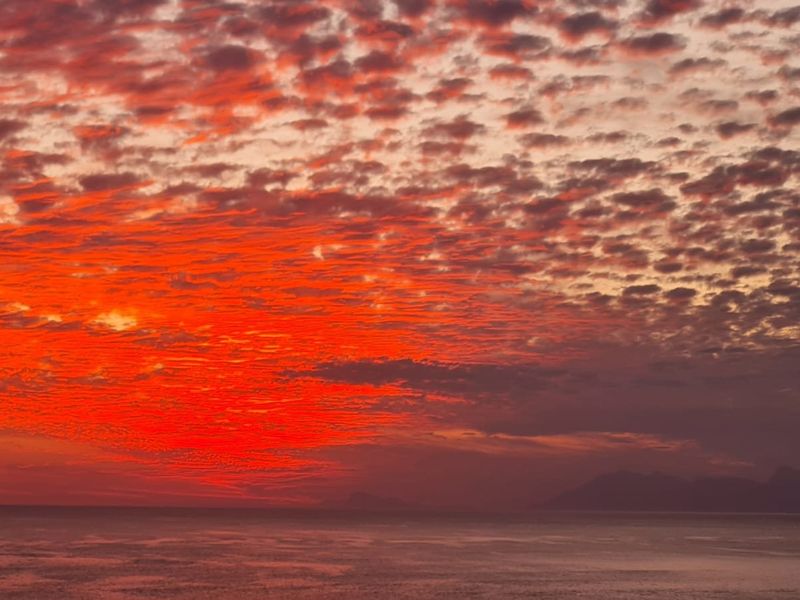 A scenic view of a vibrant sunset over the ocean and distant mountains.