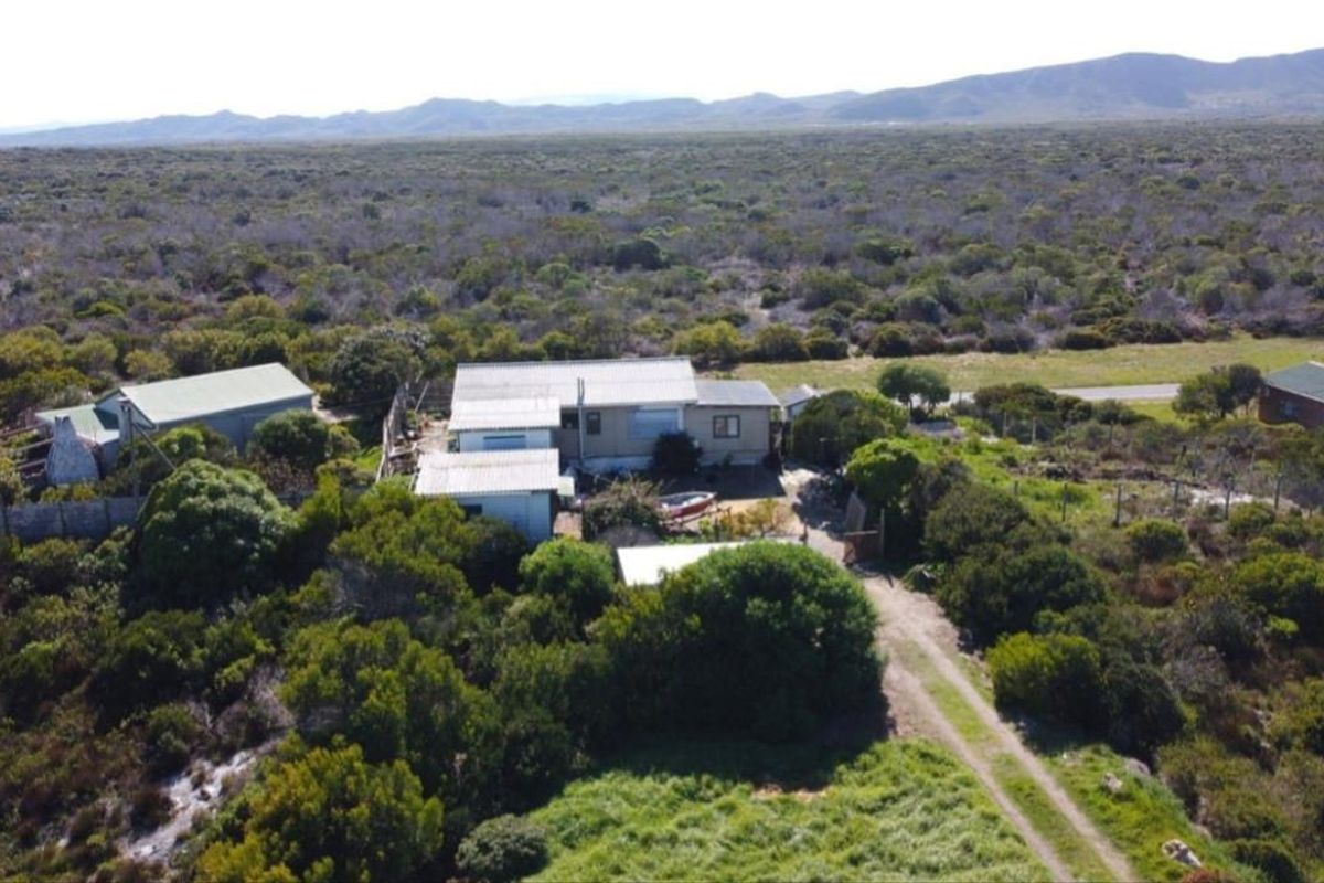 Aerial view of a rural farm property featuring multiple structures, surrounding natural vegetation, and a gravel access path.