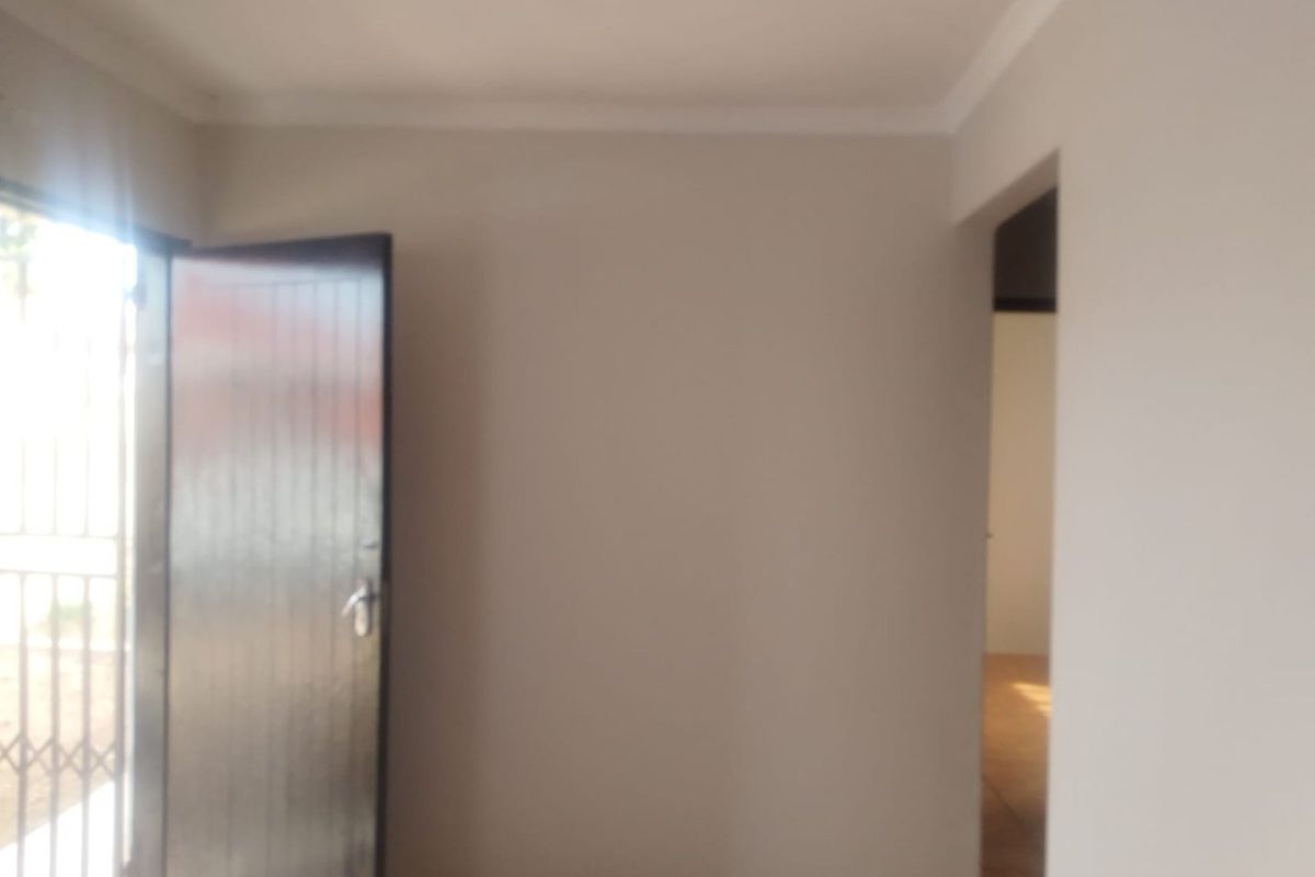 An empty living area featuring tiled flooring, neutral walls, and a security gate leading to the exterior.