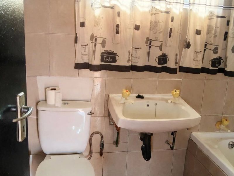 A functional bathroom featuring a wall-mounted basin, toilet, and bathtub with neutral ceramic tiling throughout.