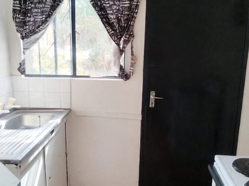 A compact kitchen featuring a stainless steel sink, tiled flooring, and a built-in stove, offering a functional space with potential for cosmetic updates.