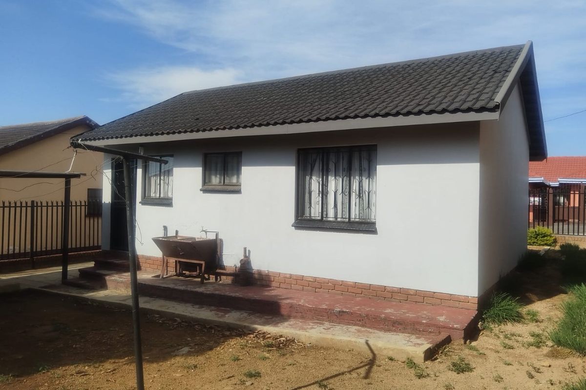 Rear view of a detached house featuring a tiled roof, security bars on windows, and a concrete patio area with an external tap.
