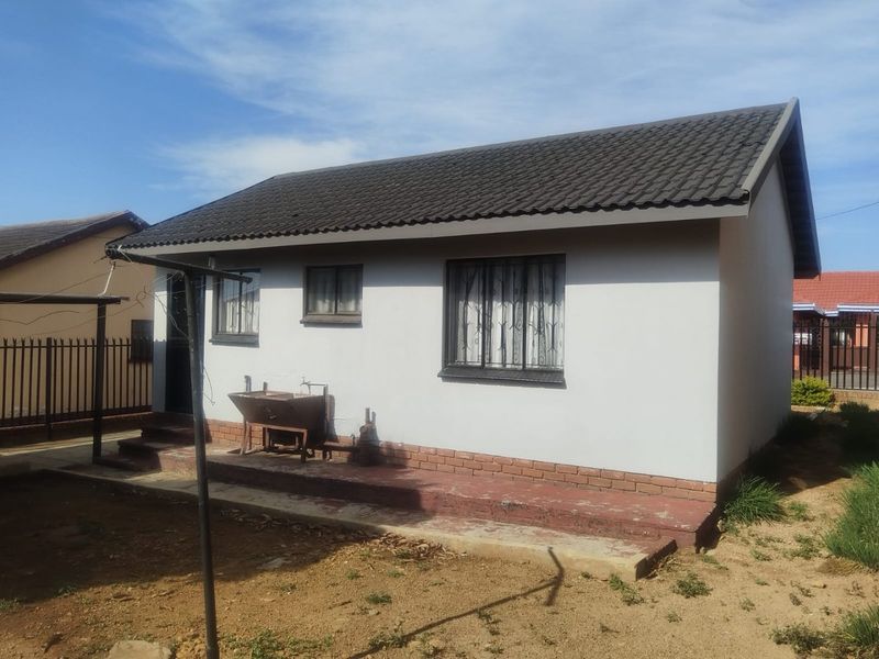 Rear view of a detached house featuring a tiled roof, security bars on windows, and a concrete patio area with an external tap.