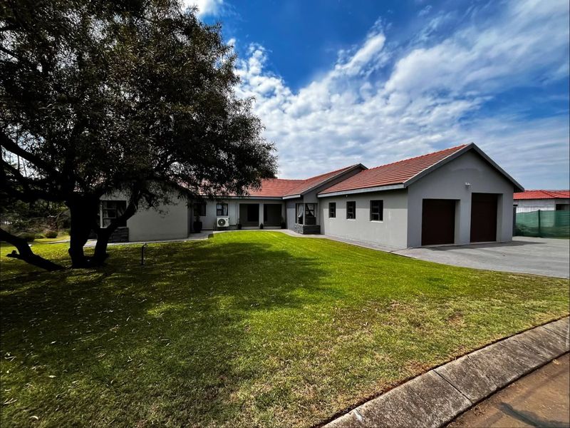 A well-maintained single-story house featuring a double garage, tiled roof, and a spacious front lawn with a paved driveway.
