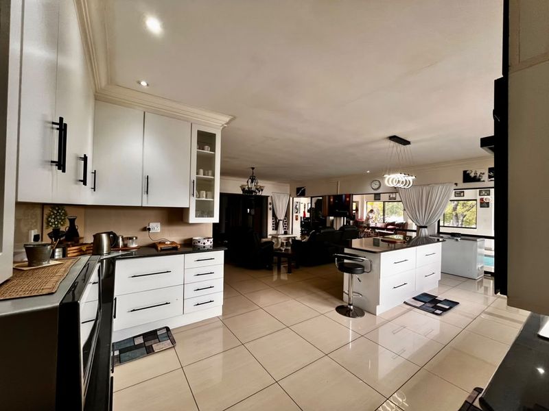 Spacious open-plan kitchen and living area featuring modern white cabinetry, a central island with stone countertops, and sleek tiled flooring throughout.
