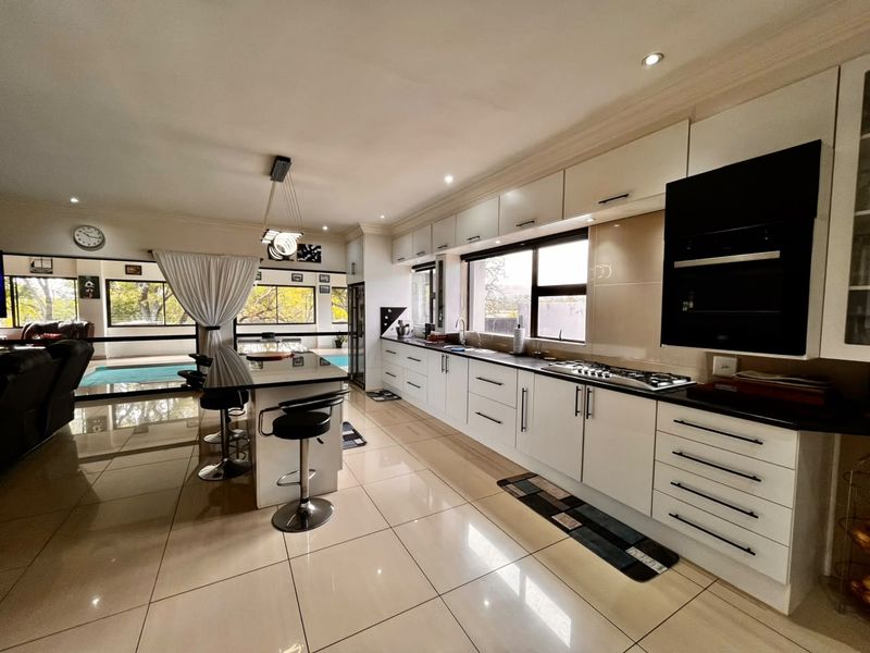 Spacious open-plan kitchen featuring modern white cabinetry, a central island with seating, integrated appliances, and large sliding doors opening to the pool area.