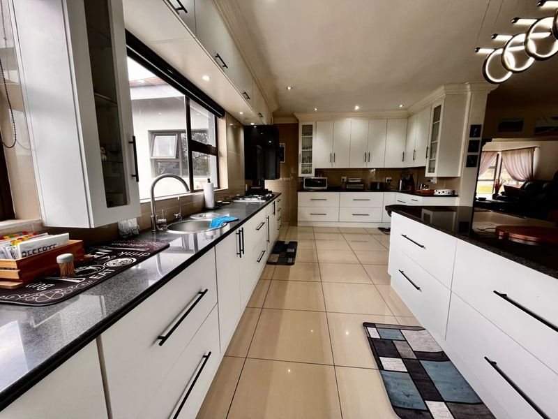 Modern kitchen featuring white cabinetry, granite countertops, integrated appliances, and tiled flooring with ample workspace and recessed lighting.