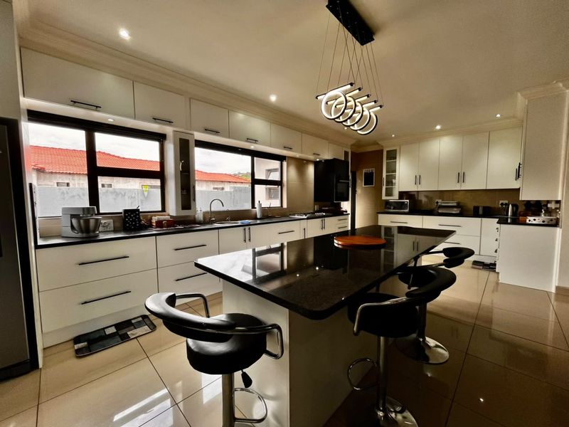 A modern, well-appointed kitchen featuring sleek white cabinetry, contrasting black granite countertops, a central island, and contemporary pendant lighting.