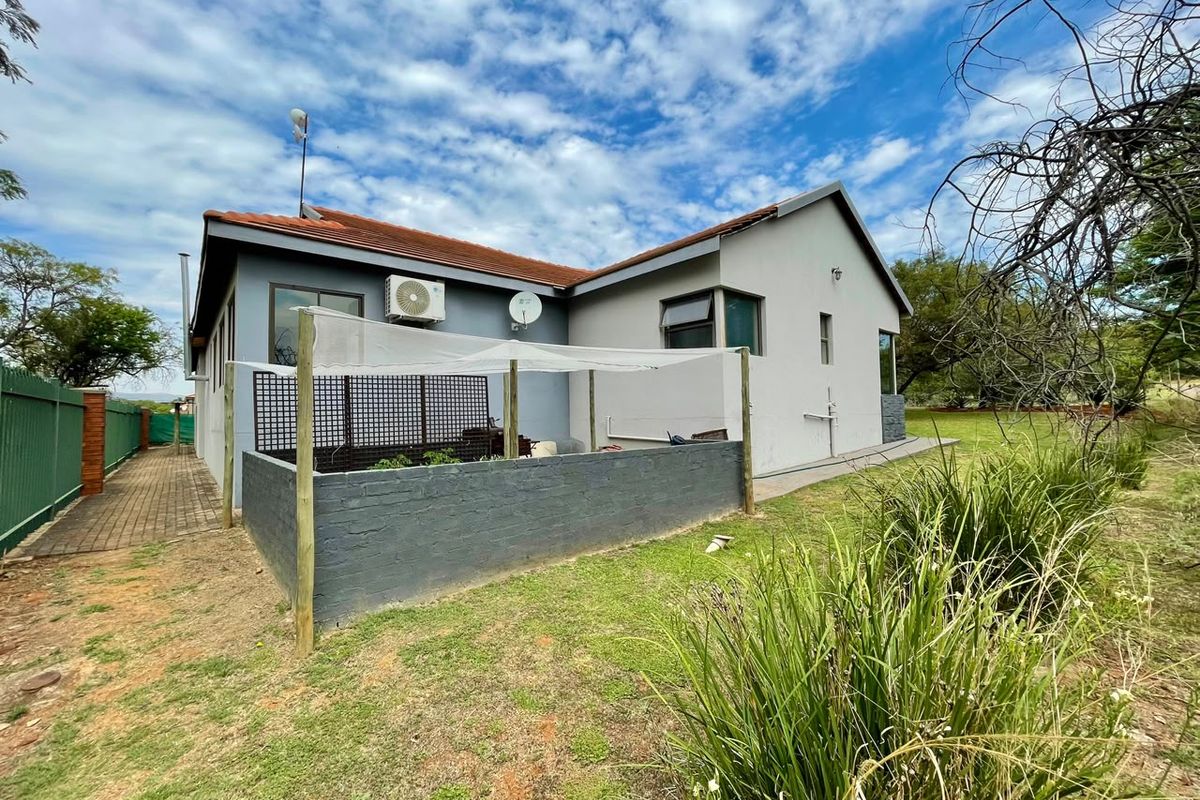 Rear view of the property featuring a tiled roof, exterior air conditioning unit, paved side walkway, and a low brick boundary wall in the garden.