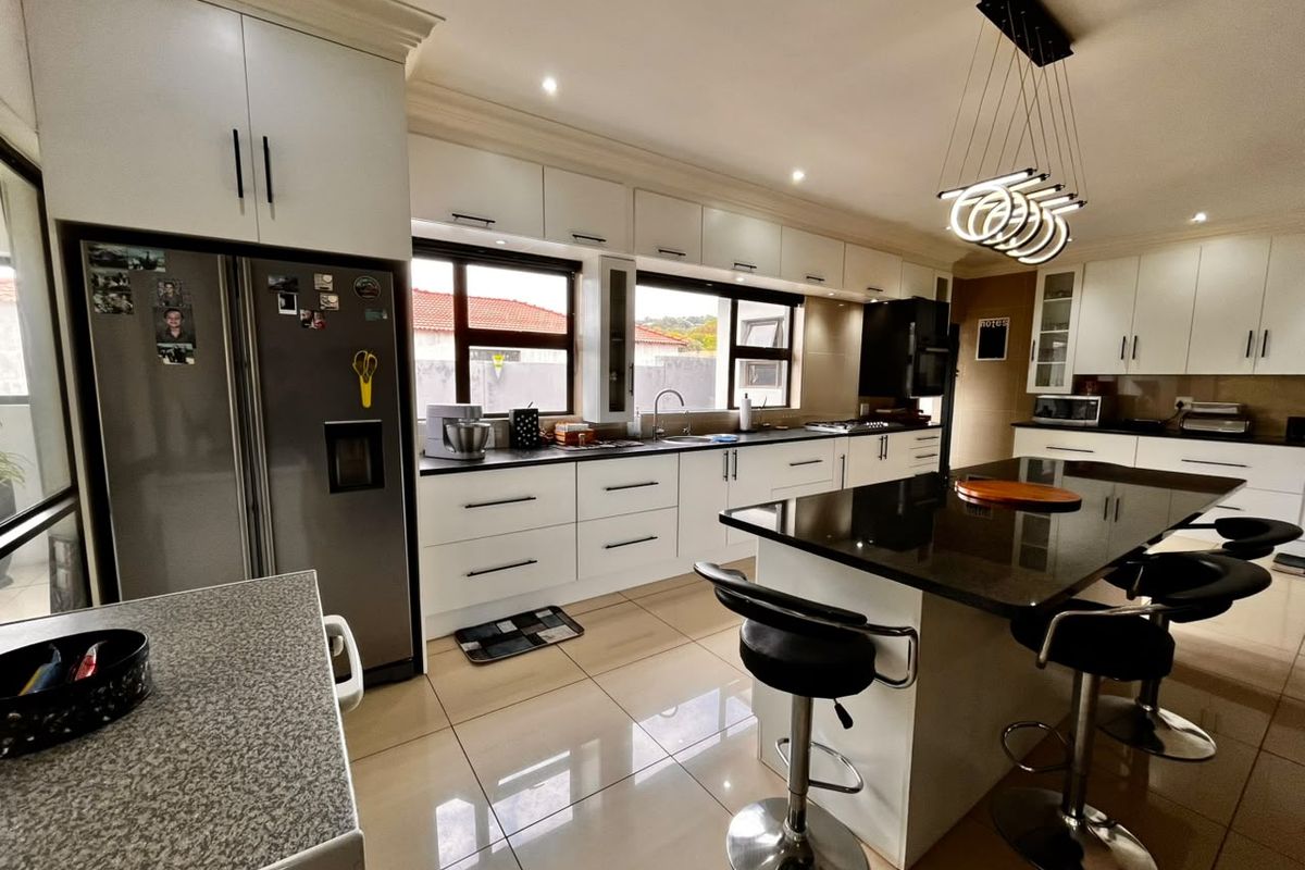 A modern, well-appointed kitchen featuring sleek white cabinetry, dark granite countertops, a central island with breakfast bar seating, and polished tiled flooring.