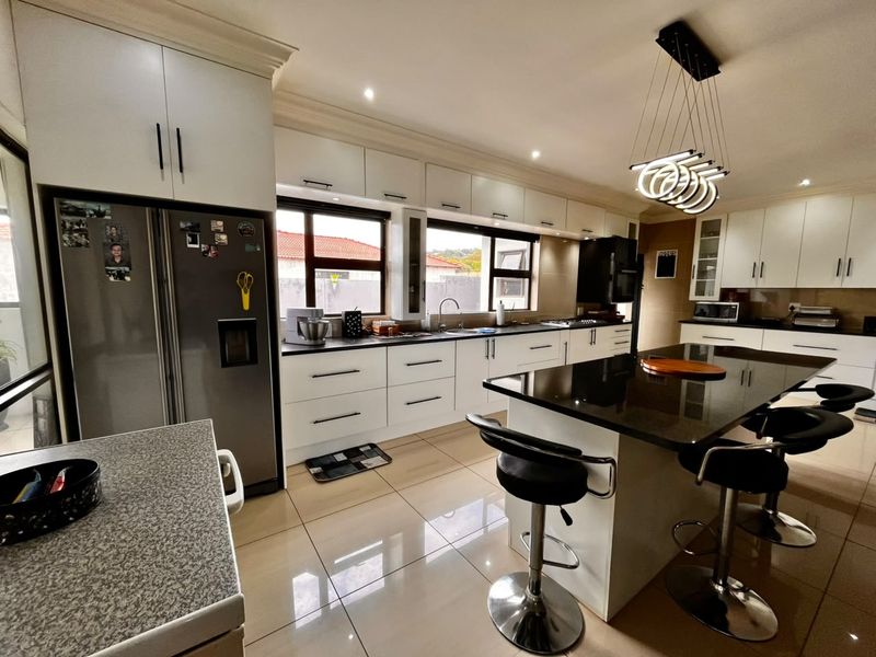 A modern, well-appointed kitchen featuring sleek white cabinetry, dark granite countertops, a central island with breakfast bar seating, and polished tiled flooring.