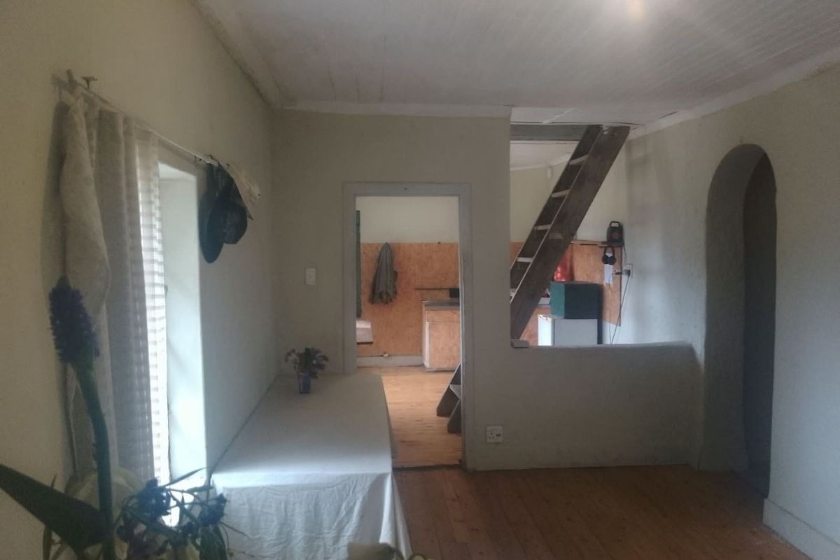 An open-plan living area featuring timber flooring, a wooden staircase, and an arched doorway, currently in need of cosmetic renovation and finishing.