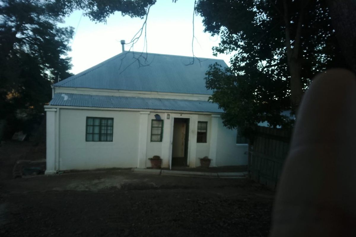 Rear view of a single-story residential property featuring a corrugated metal roof and masonry walls, set within a garden area.