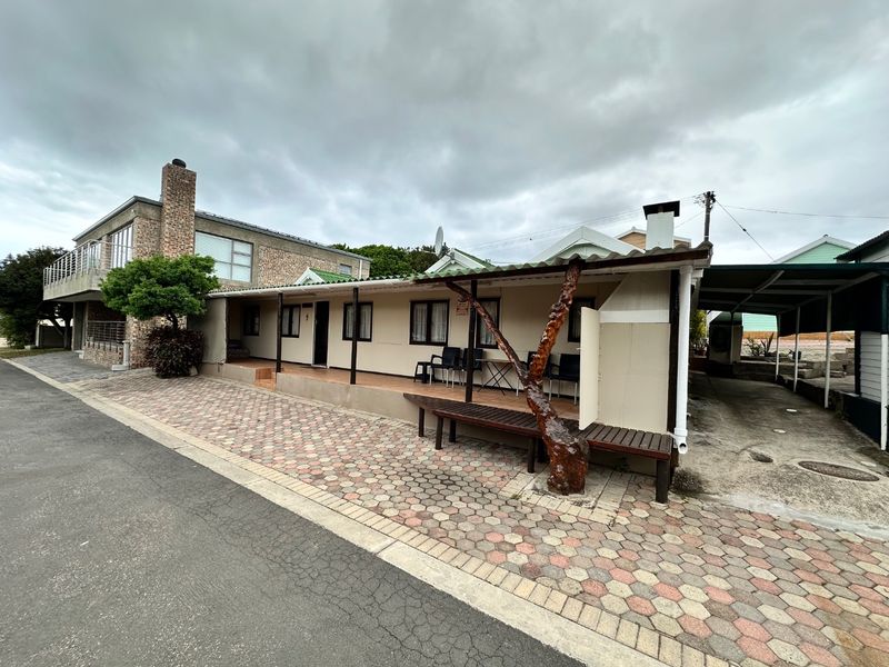 Front exterior view of a single-story house featuring a covered patio, paved driveway, and adjacent carport area under a cloudy sky.