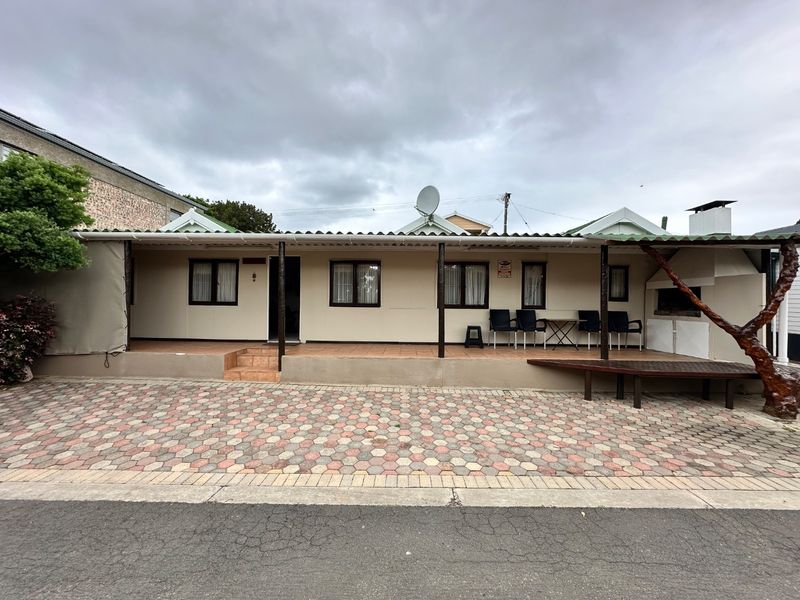 Front exterior view featuring a covered patio with tiled flooring, a built-in braai, and a paved driveway area.
