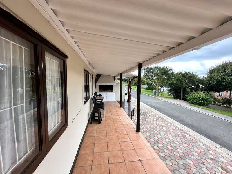 A covered outdoor patio featuring tiled flooring and a built-in braai, providing a functional space for outdoor entertaining adjacent to the driveway.
