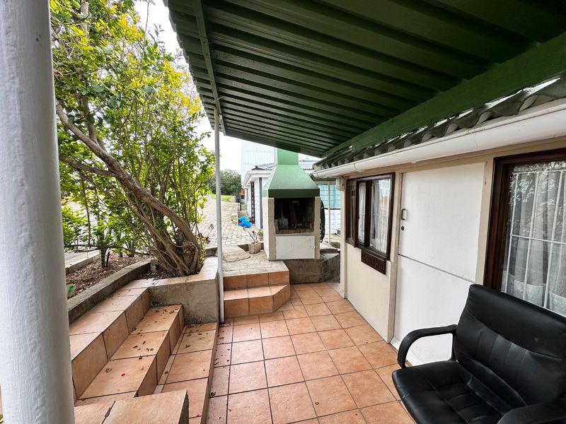 Covered outdoor patio area featuring a built-in braai, tiled flooring, and stepped terrace access, providing a functional space for outdoor entertaining.