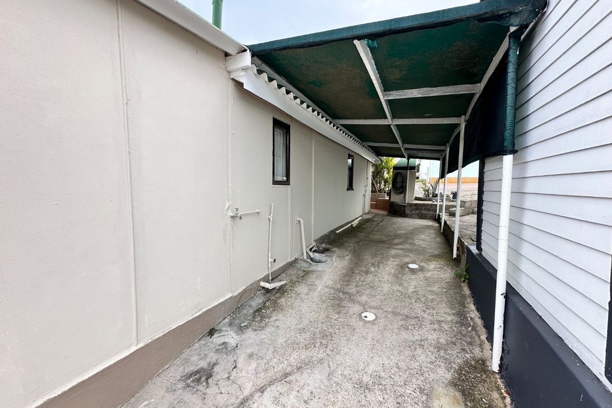 A narrow, covered rear patio area featuring concrete paving, external plumbing fixtures, and weatherboard siding, providing a functional utility space.