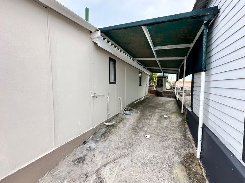 A narrow, covered rear patio area featuring concrete paving, external plumbing fixtures, and weatherboard siding, providing a functional utility space.