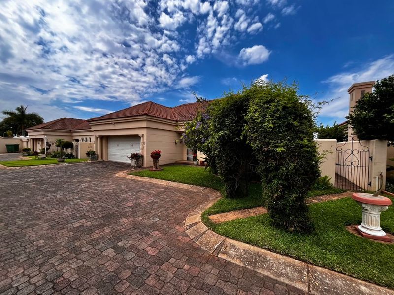 A well-maintained front exterior featuring a paved driveway, tiled roof, and landscaped garden with a secure wrought iron gate entrance.