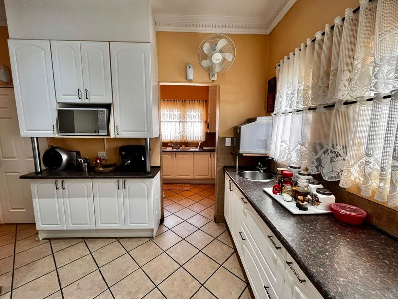 A functional kitchen featuring white cabinetry, dark laminate countertops, tiled flooring, and a convenient adjoining scullery area.