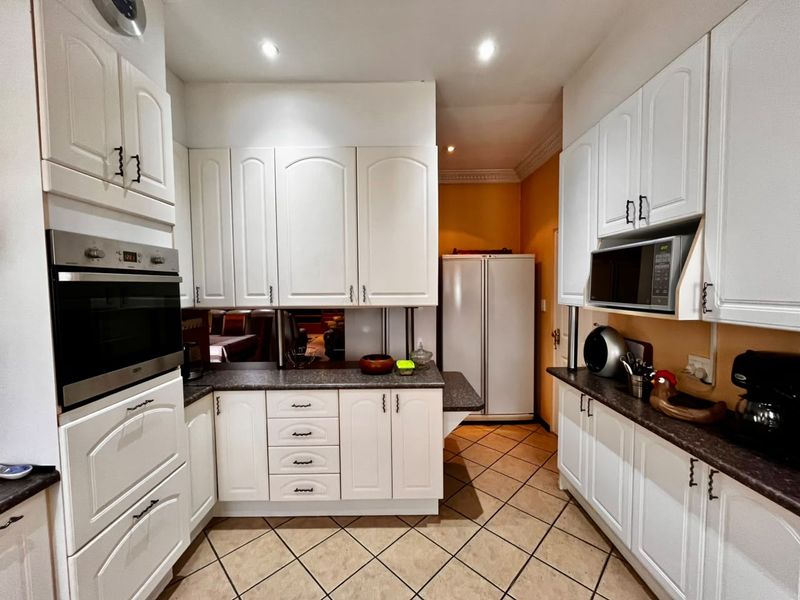 A functional kitchen featuring white cabinetry, dark laminate countertops, built-in oven and microwave, and tiled flooring.