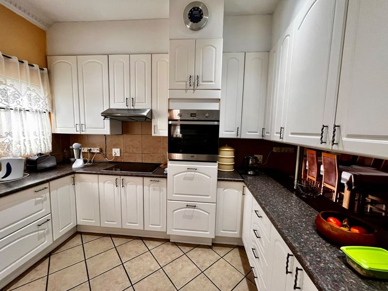 A functional kitchen featuring white cabinetry, dark laminate countertops, a built-in oven, electric hob, and tiled flooring with a neutral backsplash.