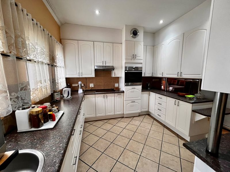 A functional kitchen featuring white cabinetry, dark laminate countertops, built-in oven, extractor fan, and tiled flooring with recessed lighting.