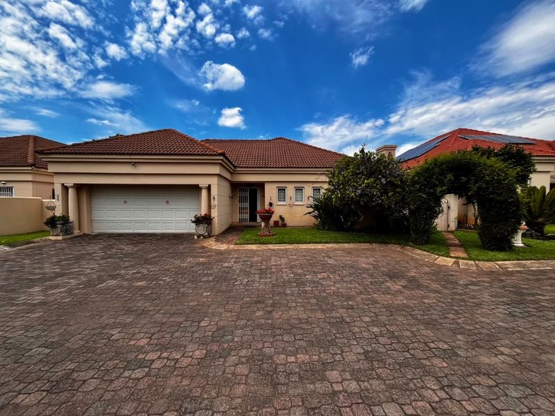 Front elevation of a well-maintained single-story house featuring a paved driveway, double garage, and established garden with a decorative archway.