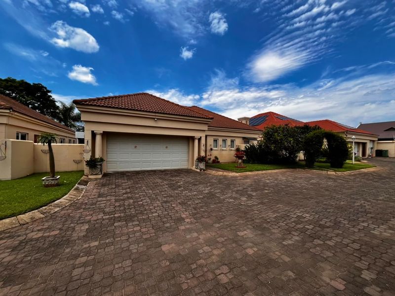 Front view of a well-maintained house featuring a paved driveway, double garage, and tiled roof with integrated solar panels.