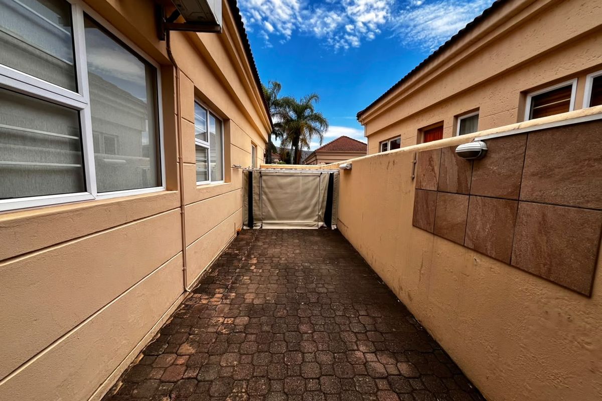A narrow paved side passage between two residential buildings, featuring boundary walls, external lighting, and an air conditioning unit.