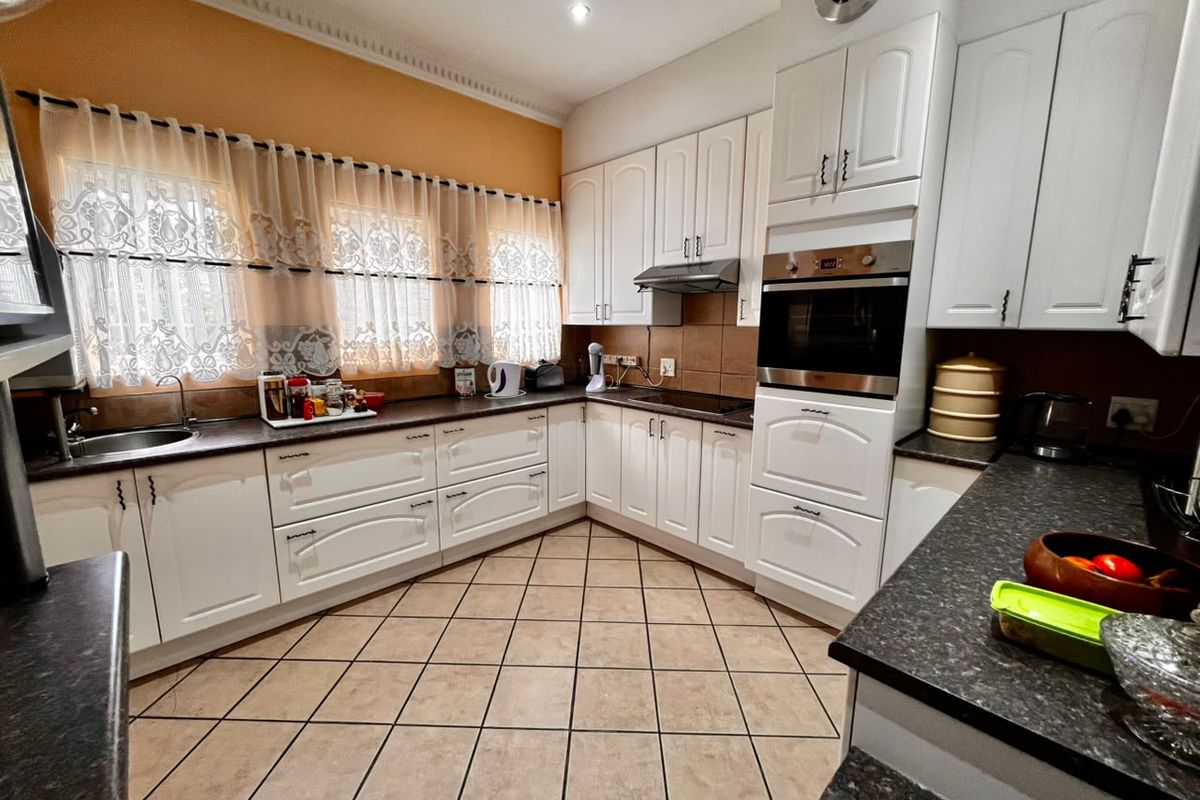 A functional kitchen featuring white cabinetry, dark laminate countertops, built-in oven, extractor fan, and tiled flooring with a neutral backsplash.