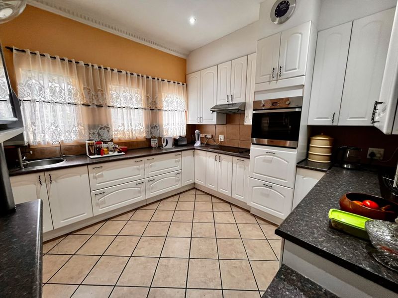 A functional kitchen featuring white cabinetry, dark laminate countertops, built-in oven, extractor fan, and tiled flooring with a neutral backsplash.